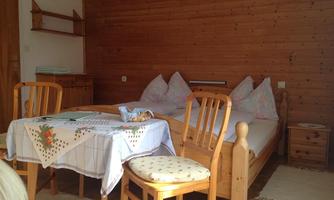 A cozy room with wood decor and a double bed. There is a table with chairs and a small shelf in the background.