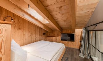 A cozy bedroom with wooden walls and a modern television. The ceiling is slanted and provides a bright, inviting atmosphere.