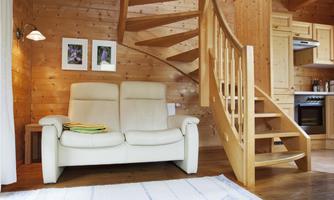A cozy living space with a bright couch and a wooden staircase. The walls are made of wood, and there are some pictures on the wall.