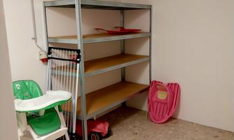 An empty room with a shelf and a high chair. A pink slide and a small toy vehicle are also visible.