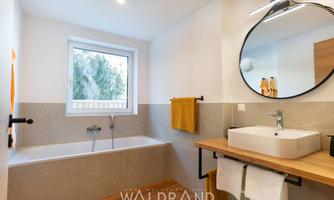 A modern bathroom with a bathtub and a sink on wood. Large windows provide plenty of light and a pleasant atmosphere.
