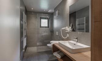 A modern bathroom with gray tiles and an elegant shower. The washing area is equipped with a stylish sink and wooden shelf.