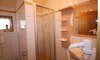 A bright bathroom with a shower and modern tiles. There is a small shelf and a hair dryer.
