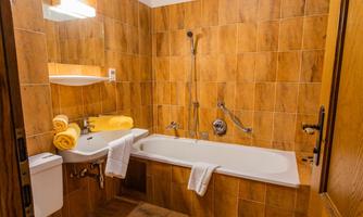 A bathroom with a bathtub and a shower. The walls are tiled in warm shades of brown, and there are towels and toiletries available.