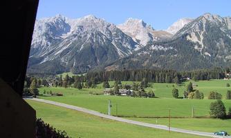 An impressive mountain landscape with snow-capped peaks and green meadows. In the foreground, a road winds through the picturesque surroundings.