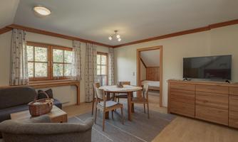 A cozy living room with a dining table and chairs. Large windows provide plenty of daylight and a pleasant atmosphere.