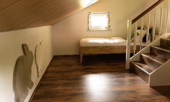 A cozy attic space with a window and a bed. The wooden stairs lead down, while animal shapes can be seen on the wall.