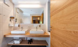 A modern bathroom with two sinks and a large mirror. The decor is stylish with wooden and tile elements.