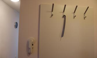 A simple hall with a white wall cabinet and several coat hooks. On one of the hooks hangs a narrow object.