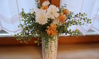 A beautiful bouquet of flowers in a white vase is on a table. The flowers are in soft colors and are framed by green foliage.