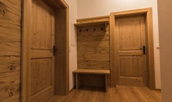 A bright hallway with wooden paneling and two doors.  
On the wall, there is a wooden bench with hooks for hanging clothes.