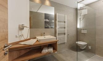 A modern bathroom with a glass enclosure and an elegant sink. The walls are in light gray tones and there are some towels nearby.