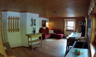 A cozy living room with wood paneling and a red couch. Next to a dining table is a small kitchenette.