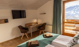 A cozy room with two beds, a desk, and a television. The windows offer a view of the mountains and nature.