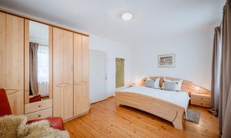 A cozy bedroom with a wooden bed and a large wardrobe. The floor is made of wood, and the walls are painted in light colors.