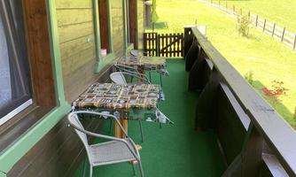 A balcony with green artificial grass and two chairs. In the background, there is a meadow and a fence.