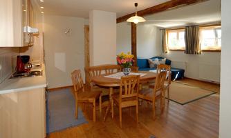 A bright, inviting kitchen with a dining table and chairs. The room has large windows that let in plenty of daylight.
