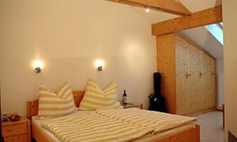 A cozy bedroom with a large bed and striped pillows. The room features light wood design and a bright, friendly atmosphere.