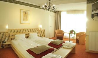 A bright room with two single beds and a cozy seating area. The room has large windows that let in plenty of daylight.