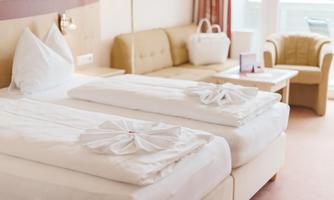 A cozy hotel room with two beds and decorative bedding. In the background, there is a sofa and a table.