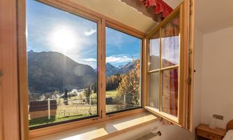 An open window overlooking majestic mountains and a clear sky landscape. The sun shines brightly over the landscape.