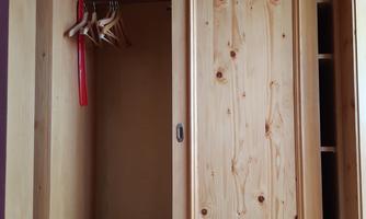 An open wooden wardrobe with an empty shelf and some hangers. The doors are made of light brown wood and the interior is simple.