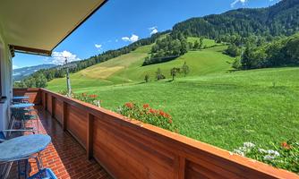 A balcony overlooking green meadows and hills. The landscape is surrounded by trees and blue sky.