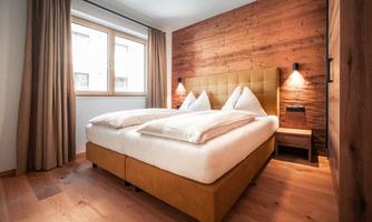 A cozy bedroom with a large bed and wood paneling. The windows let in plenty of daylight and the curtains are of a simple color tone.