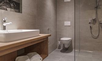 A modern bathroom with a clear glass shower and a wooden sink. The walls are in neutral gray tones, and fresh towels are ready.