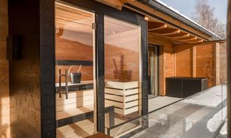 A modern wooden house with large windows and a covered terrace. The interior is simple and elegant, surrounded by natural beauty.