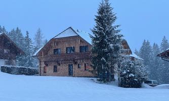 A cozy wooden house in a snowy winter landscape. The surroundings are quiet and surrounded by snow-covered trees.