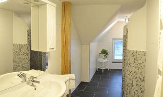 A modern bathroom with a sink and a large mirror. The walls are light tiled and the floor is laid with dark tiles.