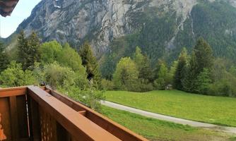 A beautiful view from a balcony of majestic mountains with snowy peaks. Below are green meadows and trees.