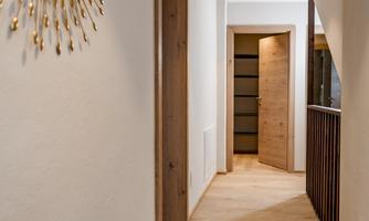 A bright hallway with a large mirror on the wall and a wooden railing. At the end of the hallway, there is an open door leading into another room.