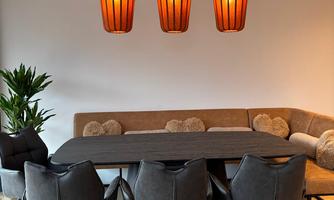 A modern dining room with a large table and comfortable chairs. Three stylish orange lamps hang above the table.