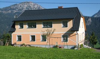 A beautiful house with a large garden and a view of the mountains. The facade is orange and the windows are green.