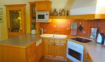 A cozy kitchen with wooden furniture and modern appliances. The walls are decorated with terracotta-colored tiles.