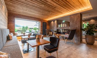 A modern café with a wooden ceiling and cozy seating areas. Large windows offer a view of the outdoor area.