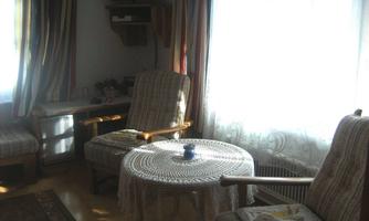 A cozy living space with two chairs and a round table. The light streams through a window, creating an inviting atmosphere.