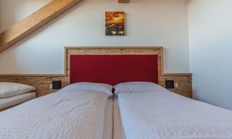 A modern bedroom with two single beds and a red headboard. On the wall hangs a picture of a landscape or a sunset.
