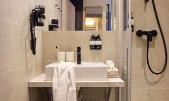 A modern bathroom with a shower and a sink. Towels and toiletries are neatly arranged on a shelf.