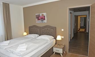 A bright and modern bedroom with a double bed and two nightstands. In the background, a door to another room is visible.