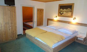 A cozy bedroom with a large bed and wooden furniture. The walls are in neutral colors and there is a television as well as a piece of artwork on the wall.