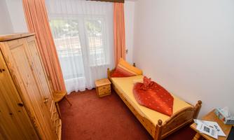 A cozy room with a single bed and wooden furniture. Large windows provide plenty of light and a friendly atmosphere.
