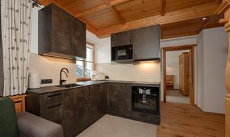 Modern kitchen with dark furniture and wooden ceiling. Bright walls and windows create a friendly atmosphere.