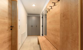 A bright hallway with a wooden bench and a coat rack on the wall. On the opposite side, there are cabinets and a door.