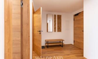 A modern entrance area with wood details. There is a bench, a mirror, and lighter walls.