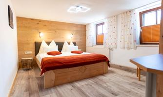 A cozy bedroom with a double bed and wooden paneling. There are large windows that let in daylight, and modern decoration.