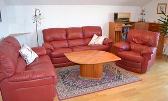 A cozy living room with red leather furniture and a round table in the middle. In the background, there are bookshelves and a plant is growing in the corner.