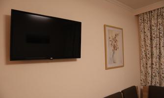 A modern television on a bright wall. Next to it hangs a decorative picture featuring a vase and flowers.